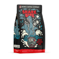 The front of a 12 ounce flavored coffee bag named Shark Bite. It showcases a skeleton riding on a shark missing an arm, and in the shark's jaws is a skeletal arm on its art.
