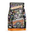 The front of a 12 ounce flavored coffee bag named Carrot Cake. It showcases a skeleton wearing rabbit ears laying down on a slice of cake holding carrots on its art.