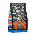 The front of a 12 ounce bag of Bones Coffee Company French Vanilla coffee. Its flavor is a creamy vanilla, and it has a skeleton wearing a beret with a black and white striped shirt drinking coffee before the Eiffel tower on the art.