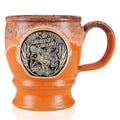 The front of the Bones Coffee Company Jacked O’ Lantern hand thrown mug. The golden medallion has the art of the Jacked O’ Lantern coffee on it. The mug is an orange finish dipped in pumpkin spice glaze.