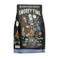 The front of a 12 ounce bag of Bones Coffee Company S’morey Time coffee. Its flavor is s’mores, and it has a skeleton holding a flashlight around a campfire with bigfoot and a werewolf on the art.